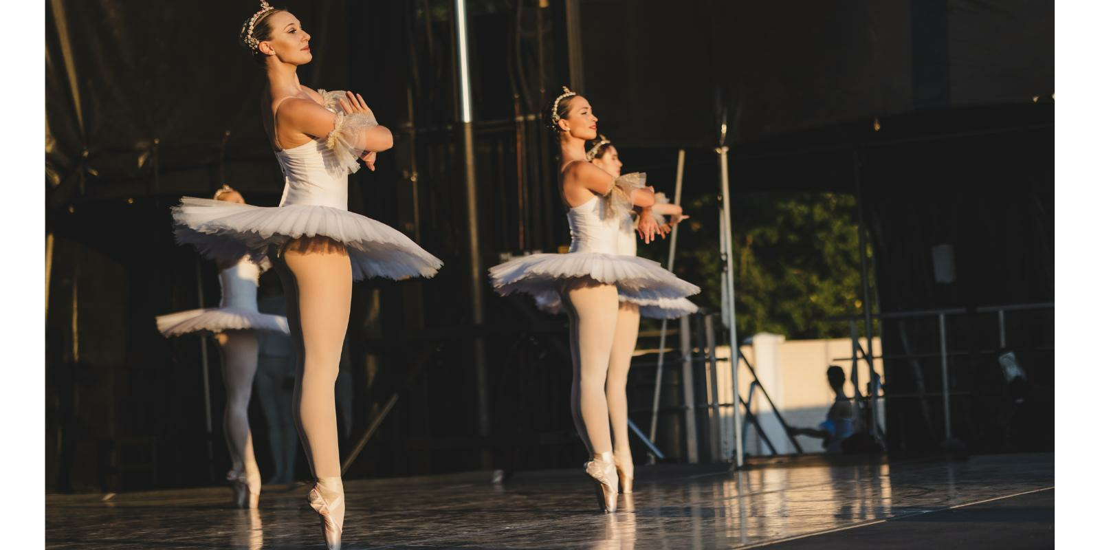 Members of First State Ballet perform on stage in white tutus and small crowns.