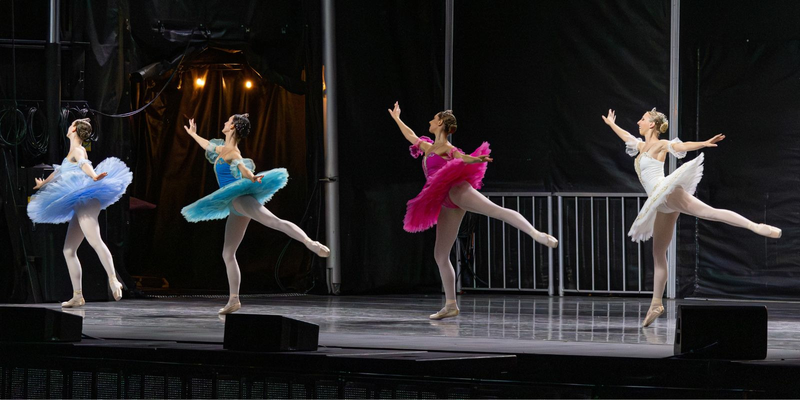 Members of First State Ballet perform on stage in white tutus and small crowns.
